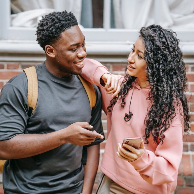 happy young diverse couple sharing smartphone on street